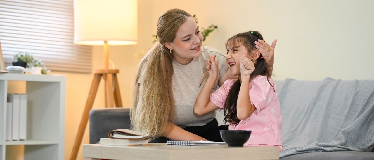 A young woman and a girl laughing and clapping together on the sofa